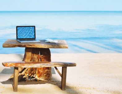 Photo d'un bureau en bois avec un ordinateur portable et la mer en arrière plan.
