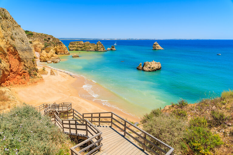 Escaliers en bois vers la célèbre plage de Praia Dona Ana avec falaises et mer turquoise en arrière plan.